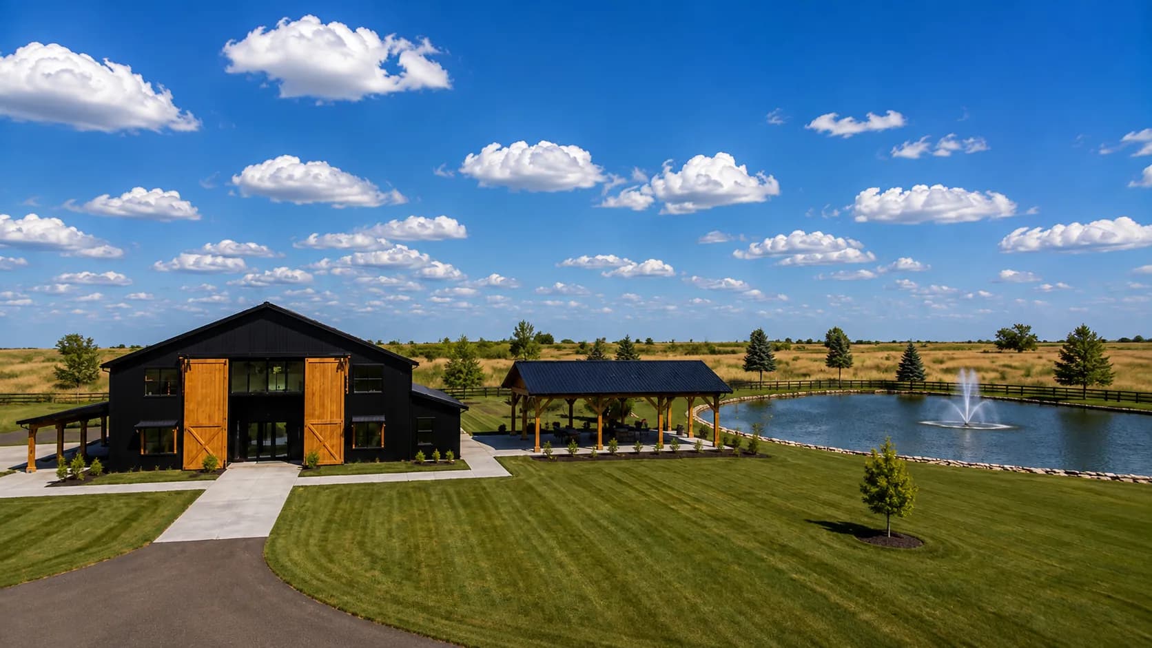Architectural rendering of Antelope Creek Ranch Venue near Wichita, Kansas: a black board-and-batten event barn with cedar doors, a covered pavilion, and a two-acre pond with a fountain set in open prairie.