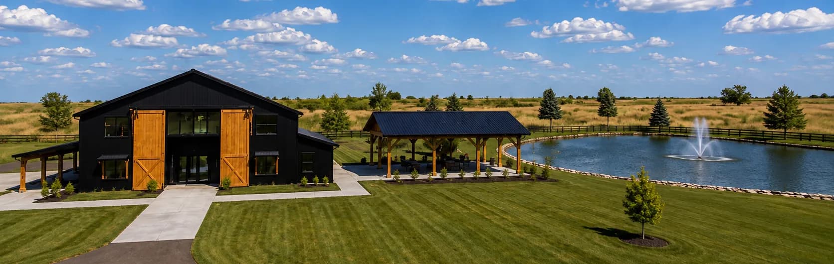 Wide architectural rendering of the grounds at Antelope Creek Ranch Venue near Wichita, Kansas: the barn, covered pavilion and two-acre pond across open prairie.